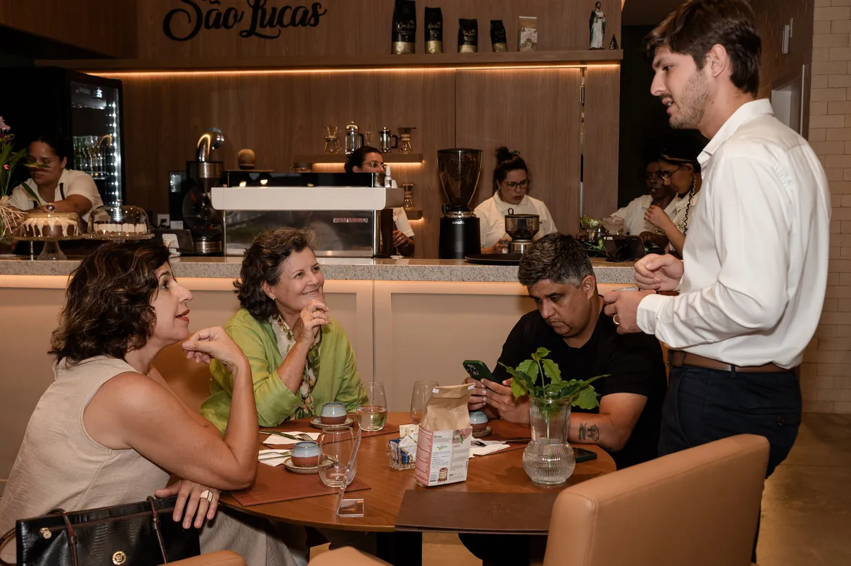 Clientes à mesa diante do balcão da Casa São Lucas, com o Lucas atendendo